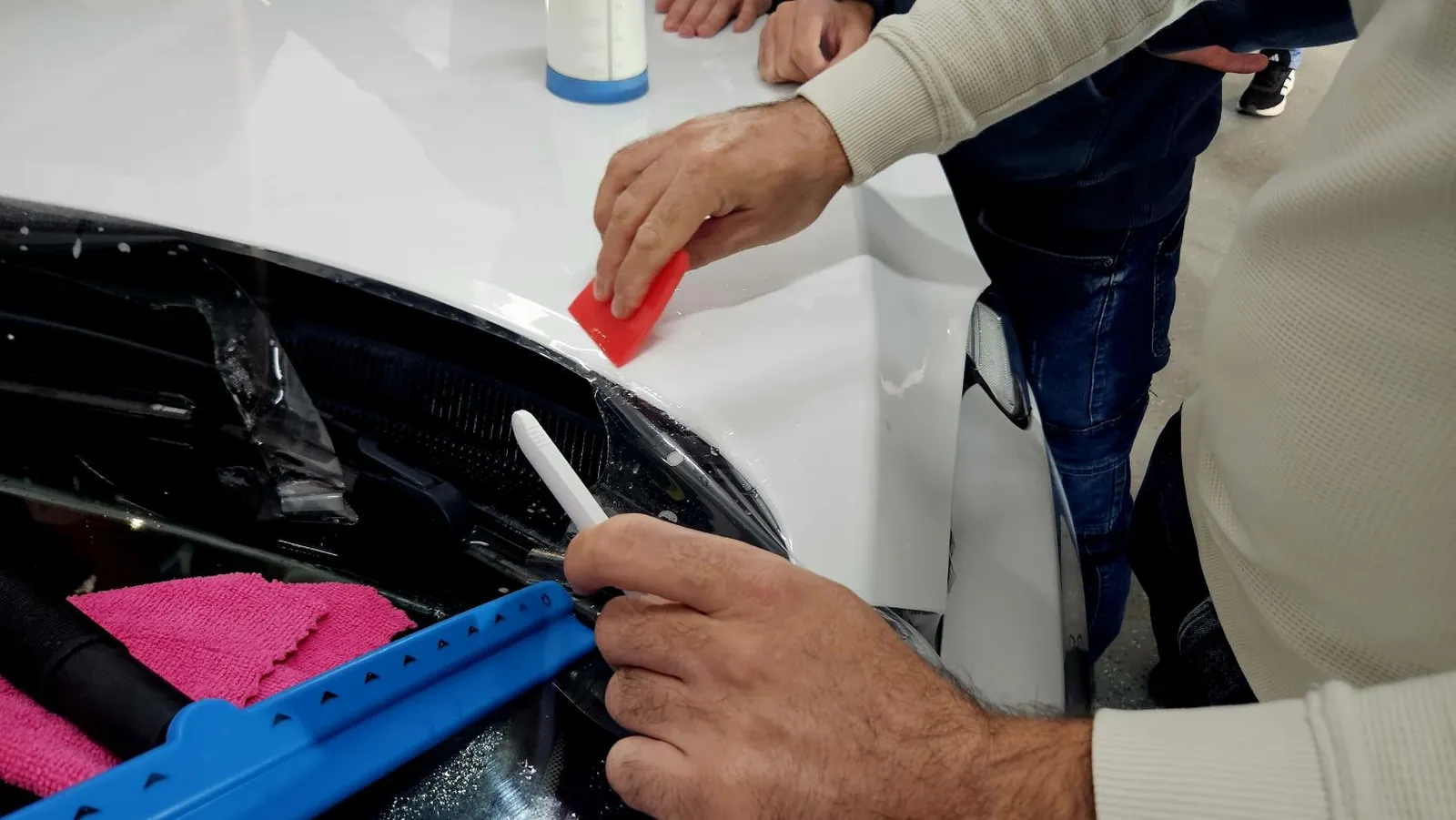 Tehnician aplicând folie auto PPF pe zona frontală a unui vehicul, folosind racletă și instrumente profesionale, în cadrul unui workshop Verla dedicat tehnicilor corecte de instalare.