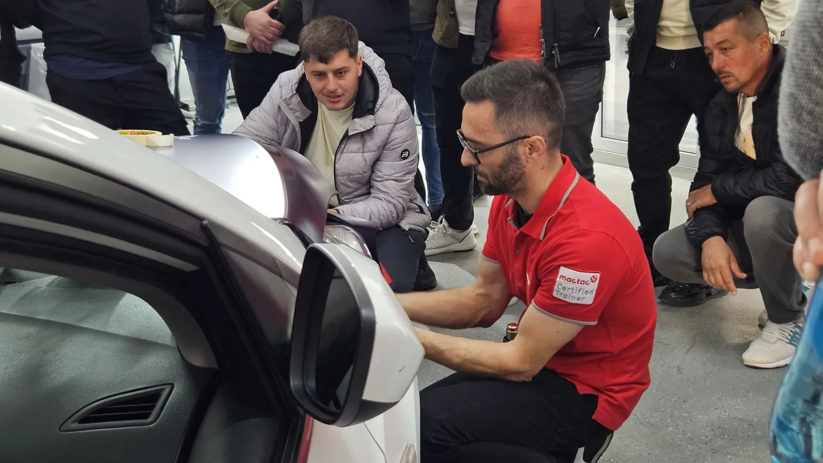 Participanți exersând aplicarea unei folii auto pe panoul frontal al unui vehicul, în cadrul workshopului Verla × Vasile Lomanar.